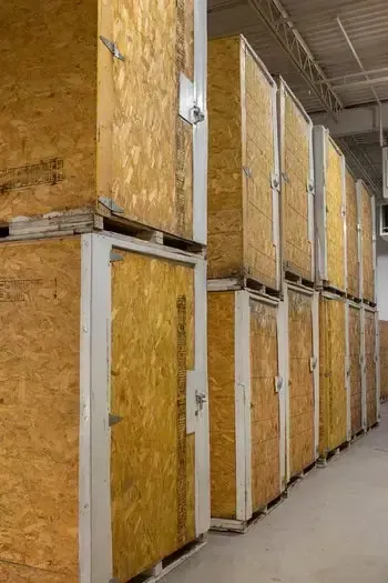 Stacked wooden shipping crates in a warehouse aisle under industrial lighting.