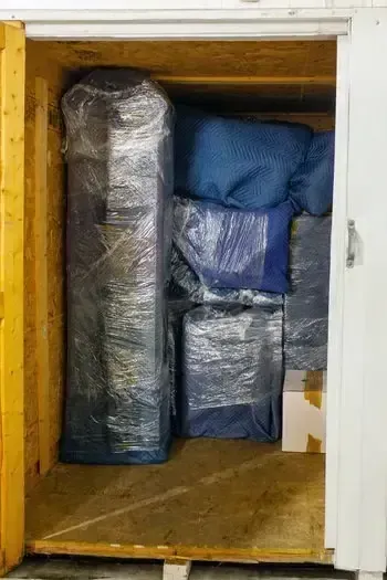 A storage closet packed with wrapped furniture and blue cushions on a wooden floor