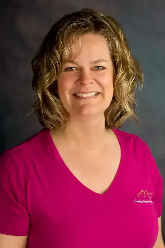 Smiling woman in a bright pink V-neck shirt against a gray studio backdrop