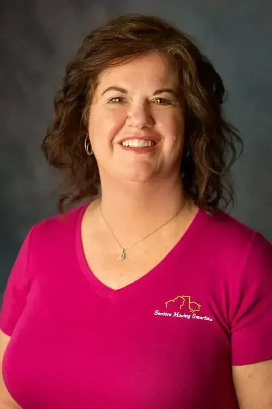 Smiling woman in a bright pink V-neck shirt against a gray studio backdrop