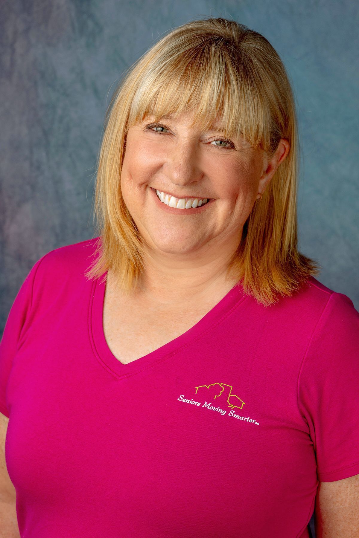 Smiling woman in a bright pink shirt against a gray-blue studio background