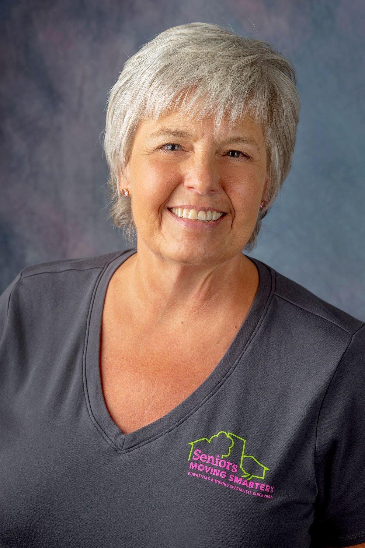Smiling woman with short gray hair in a dark gray V-neck shirt against a gray backdrop