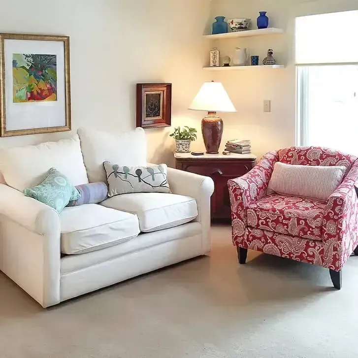 Bright living room with white sofa, red armchair, lamp, and framed wall art
