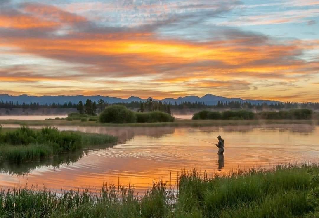 Sunset over a misty lake with a lone person fishing, orange clouds reflecting on calm water