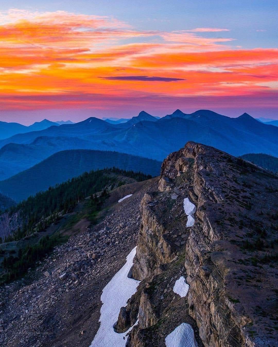 Rocky mountain ridge at sunrise with colorful pink and orange sky over layered blue peaks