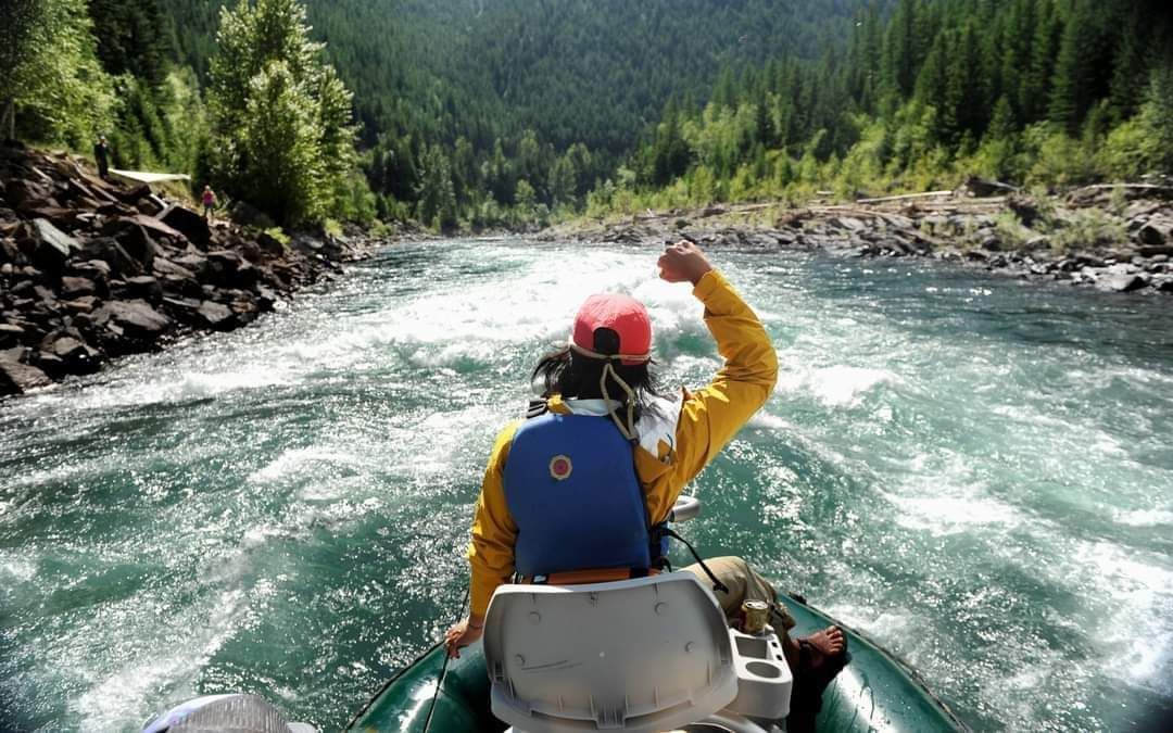 Person paddling a raft through a rocky river rapids in a forested canyon