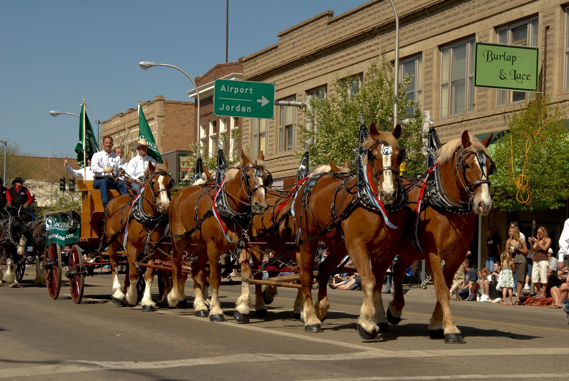 Horse-drawn carriage parade with Clydesdales pulling a decorated wagon down a city street.