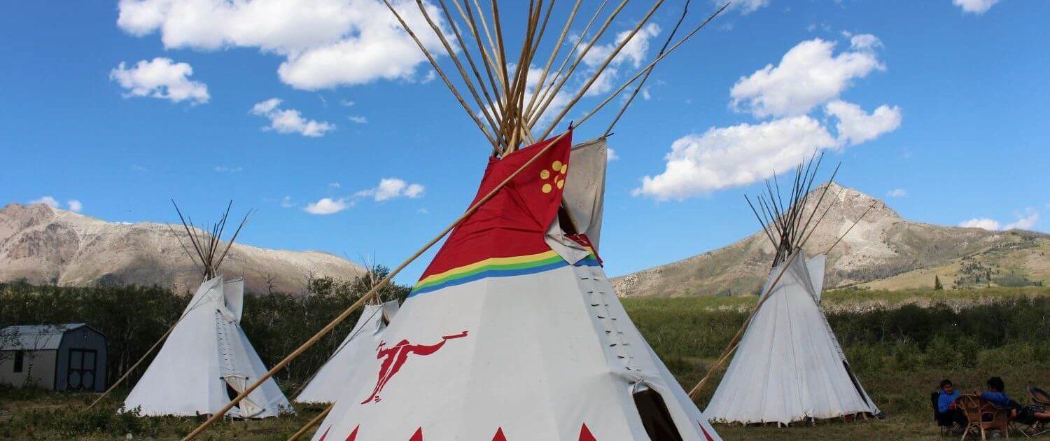Traditional teepees on grassy plain beneath blue sky, with a red and white teepee in the center
