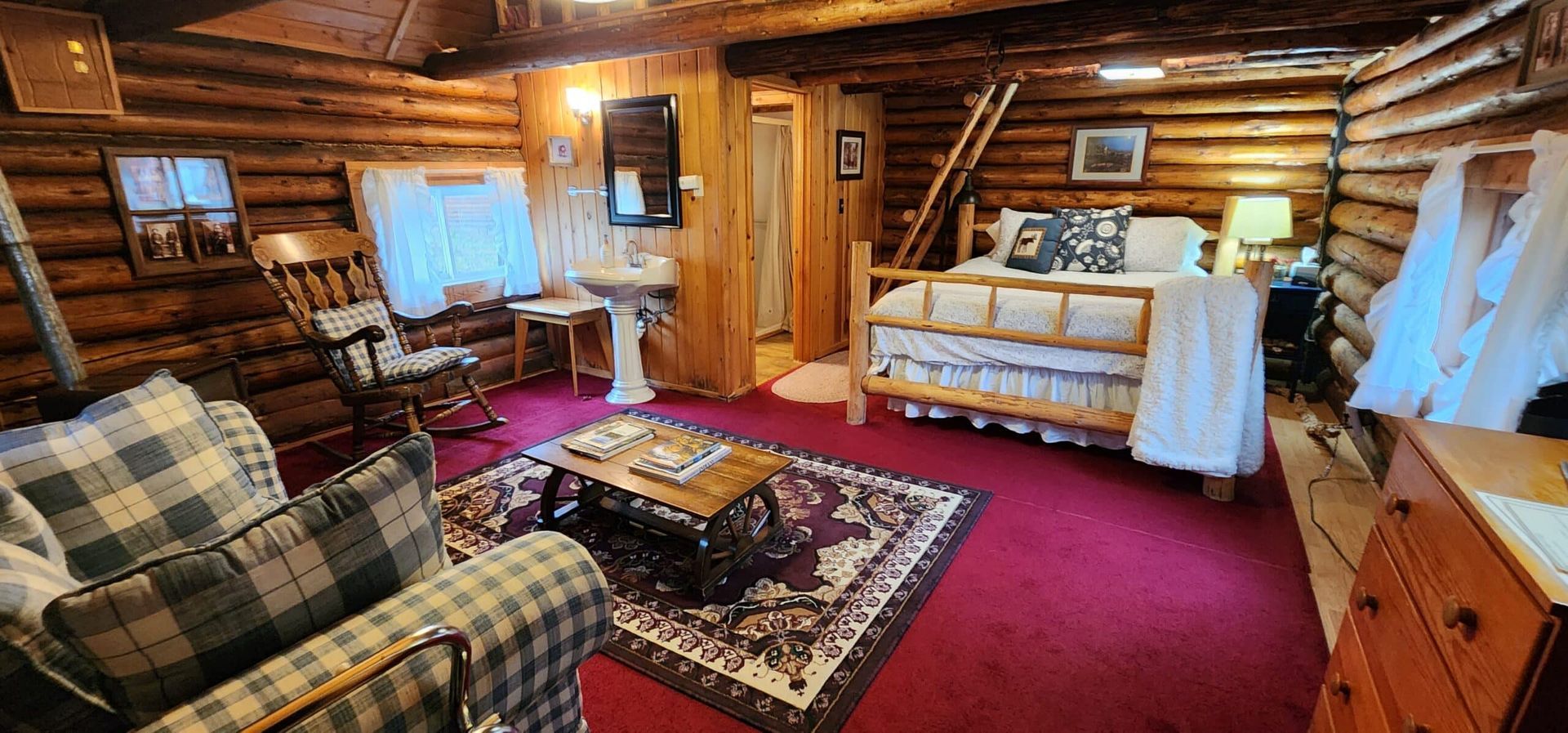 Cozy log cabin living room with plaid sofa, red rug, wooden walls, and a bed by the window
