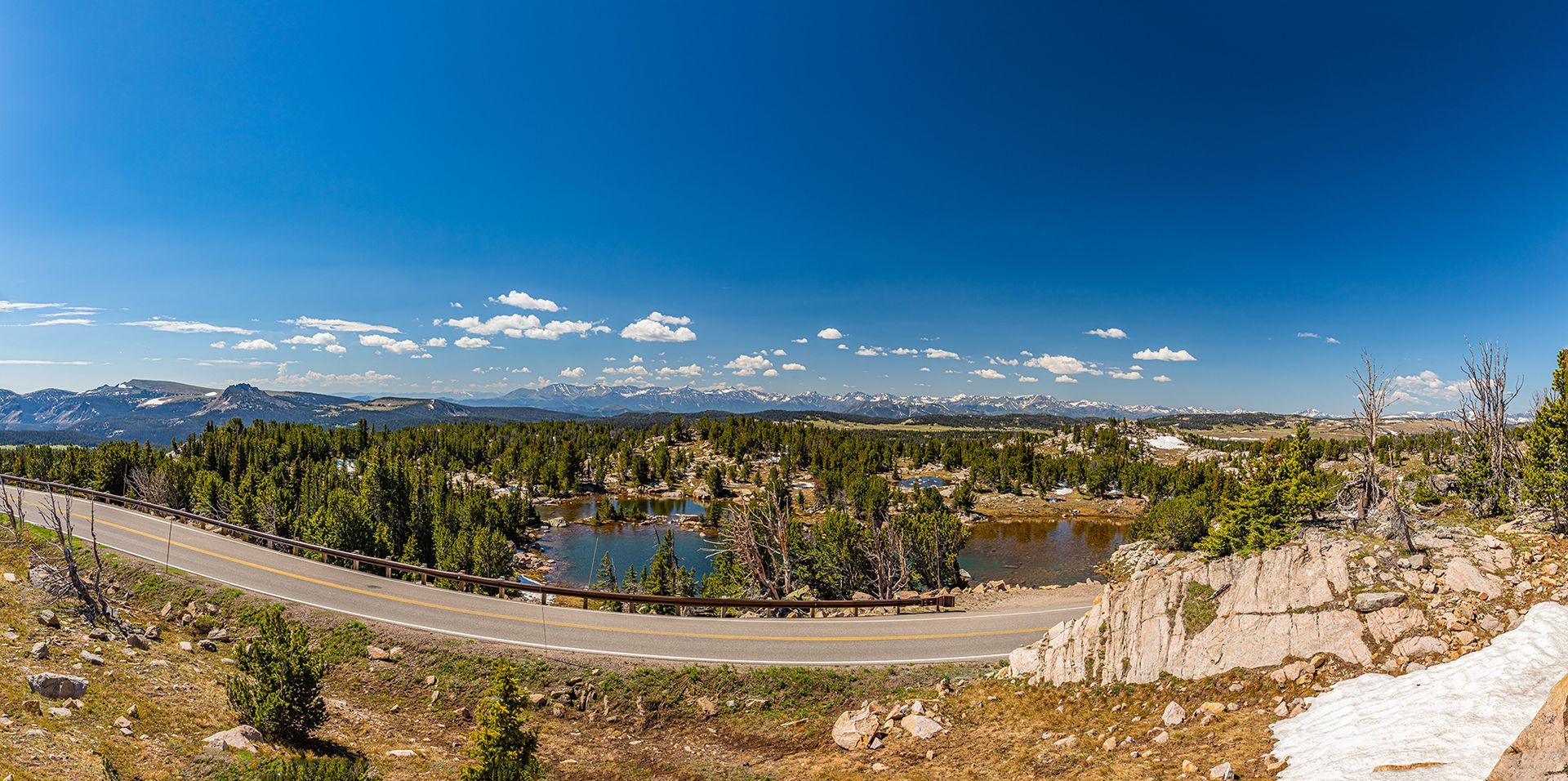 Mountain lake panorama with forest, winding road, and blue sky with clouds