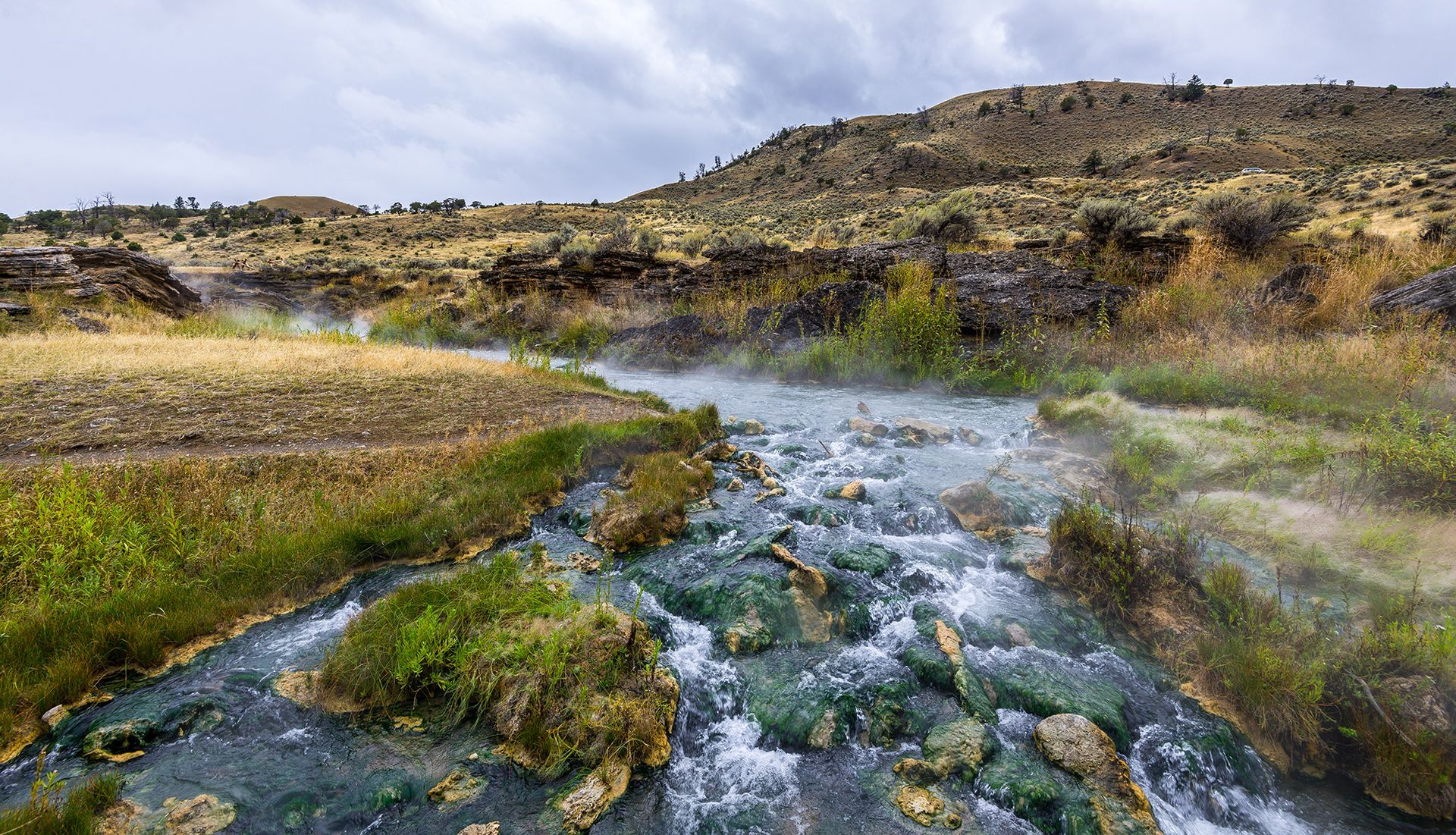 Rocky stream flowing through a grassy canyon under a cloudy sky