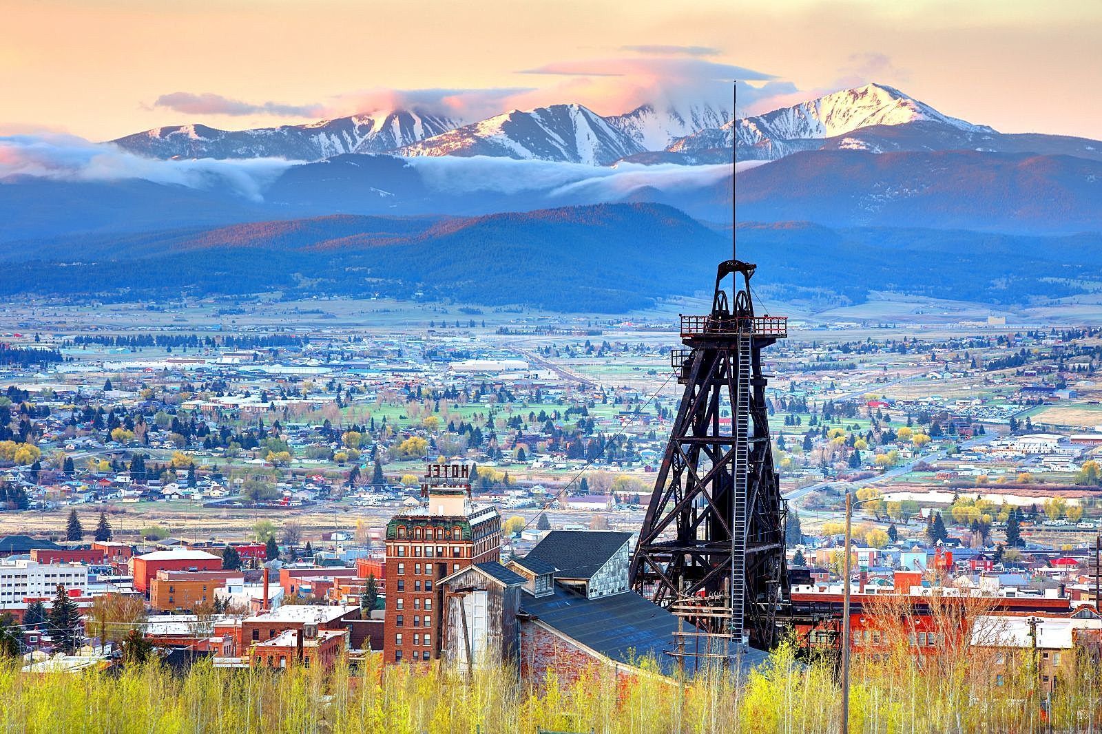Industrial tower overlooking a colorful city with snow-capped mountains in the distance at sunset