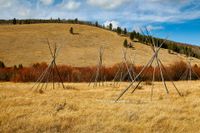 Grassy hillside with teepee-shaped wooden poles under a blue sky