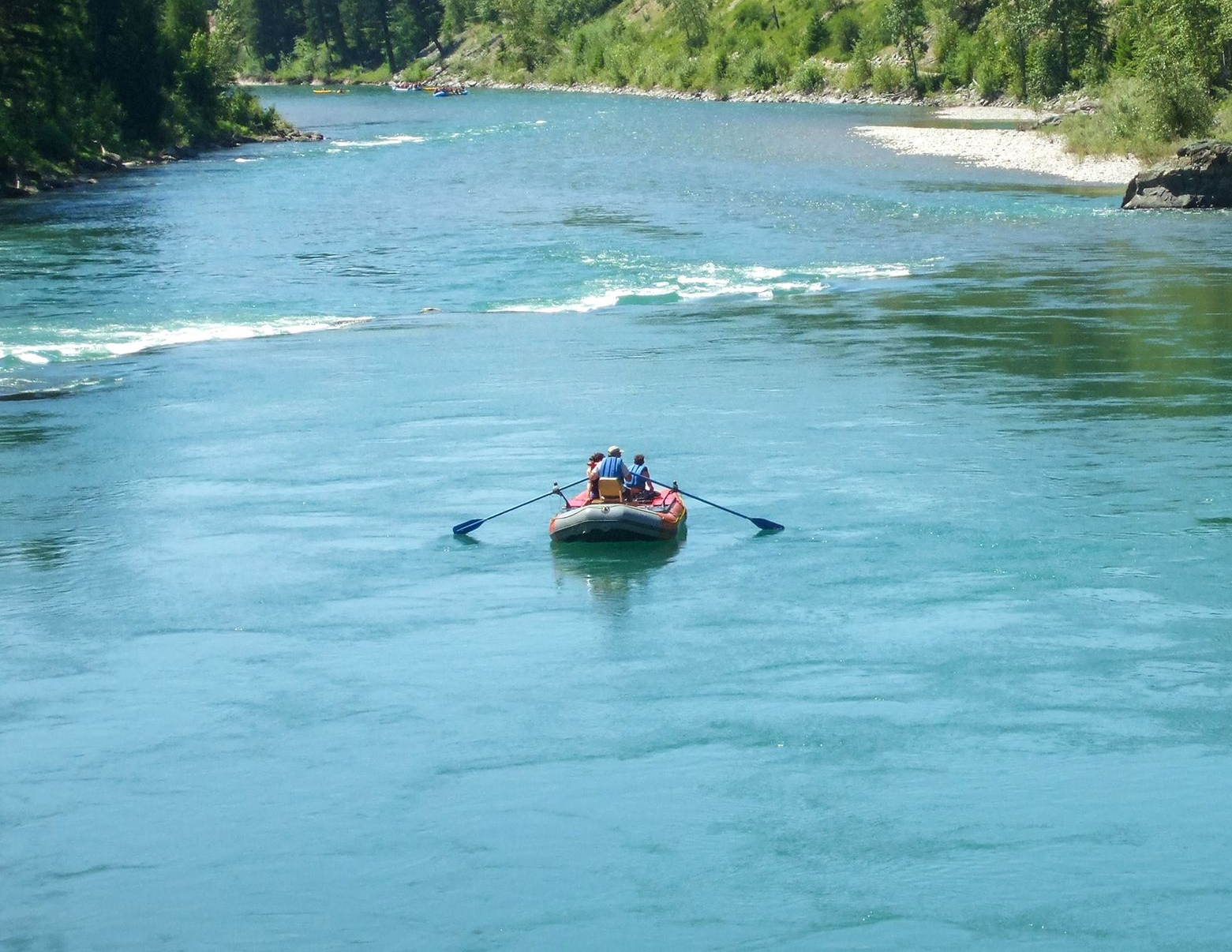 Rafting boat with paddlers on a turquoise river, surrounded by green forest banks