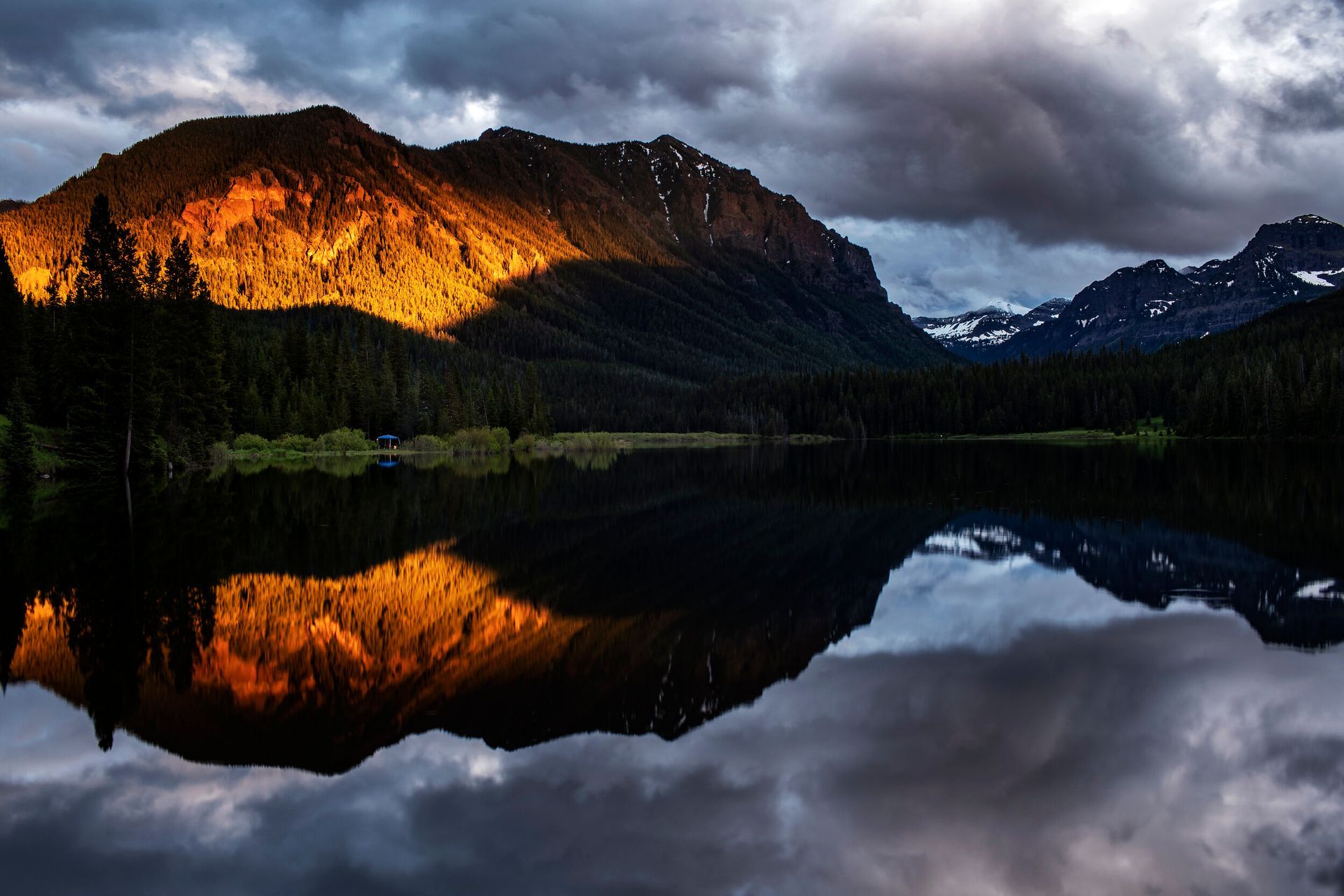 Sunlit mountain reflected in a calm lake under dark storm clouds