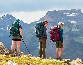Three hikers with backpacks standing on a mountain ridge overlooking snowy peaks