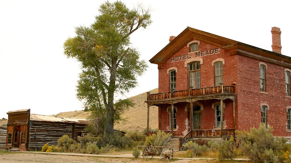 Old red brick building beside a tree in a dry, rural landscape with a weathered shed nearby
