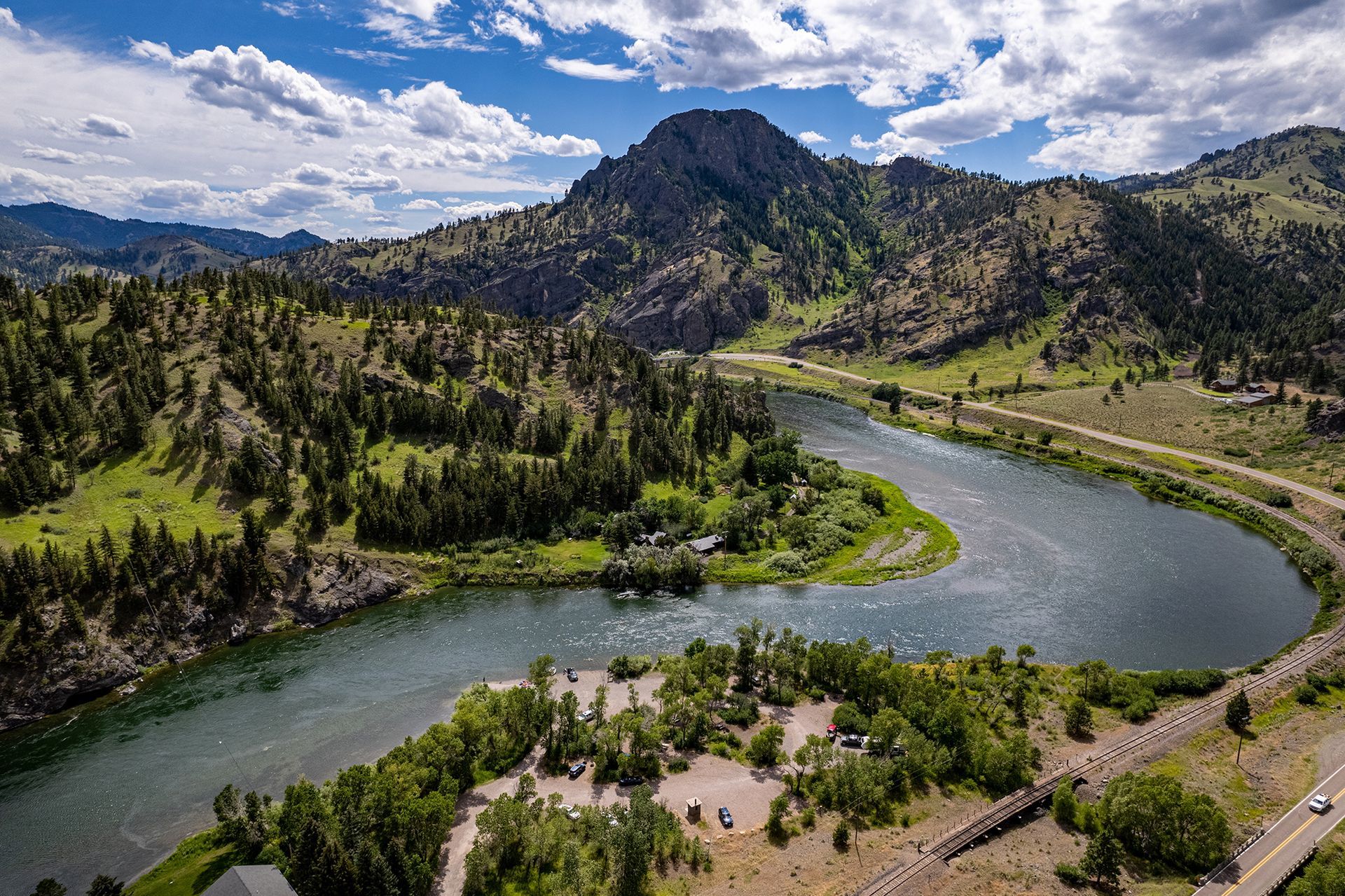 Winding river through green hills and rocky mountains under a partly cloudy blue sky