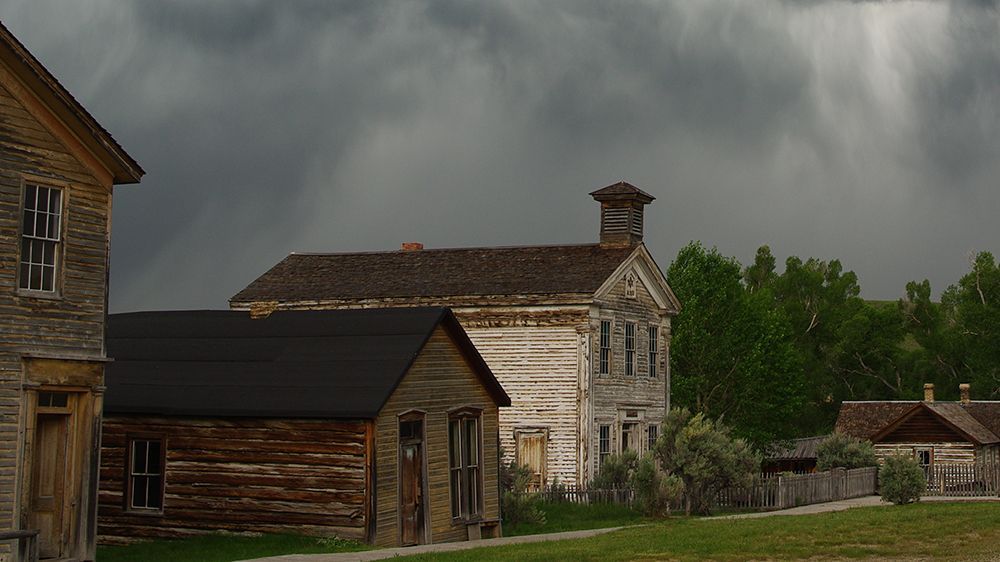 Old rustic wooden houses under a dark, stormy sky with trees and a grassy yard