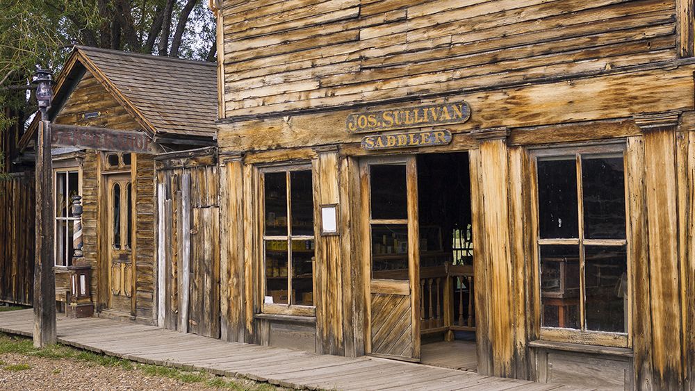 Weathered wooden Western-style building with porch, tall windows, and a sign above the entrance
