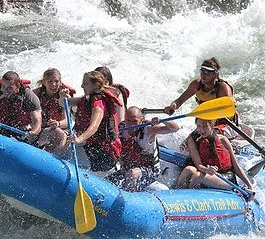 Rafting group splashes through whitewater in a blue inflatable raft with yellow paddles