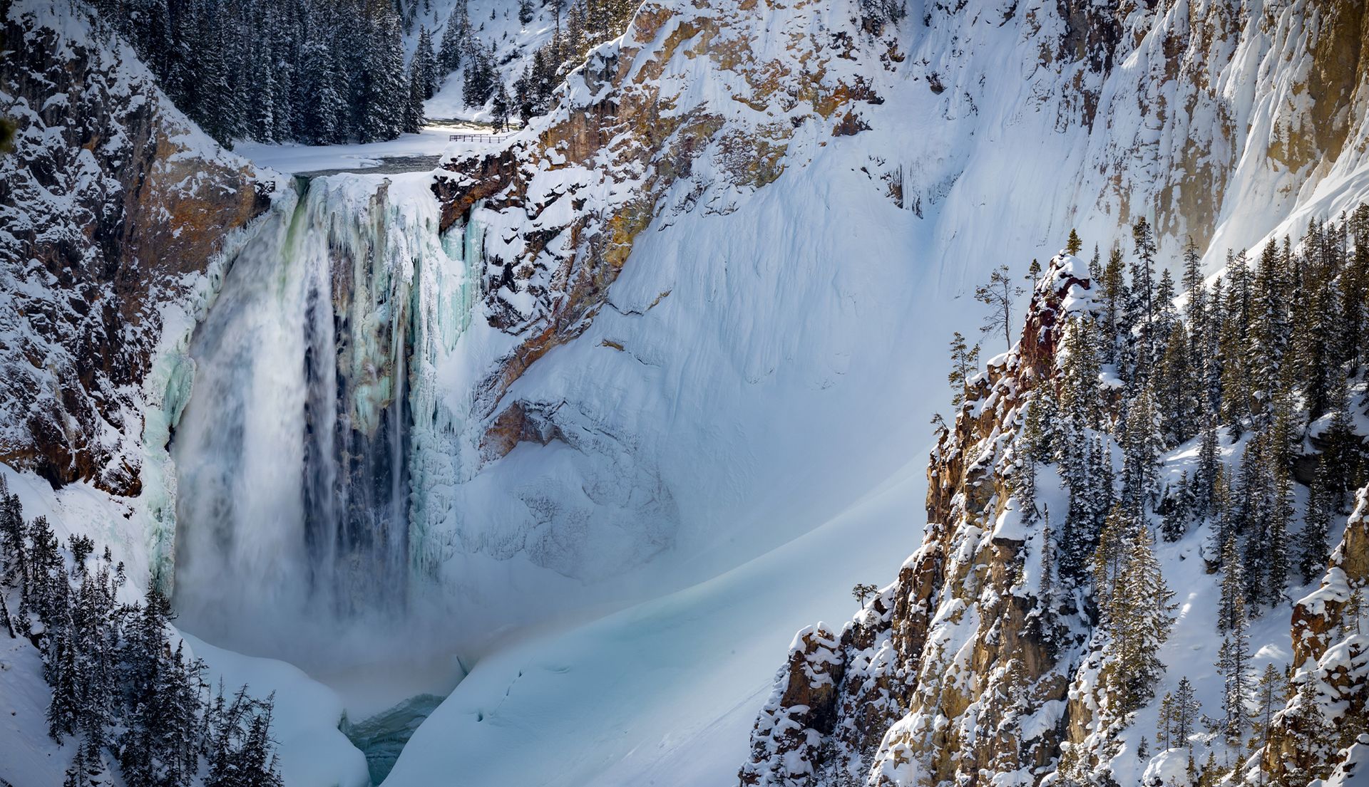 Snowy canyon with a frozen waterfall and dark evergreens on rocky cliffs