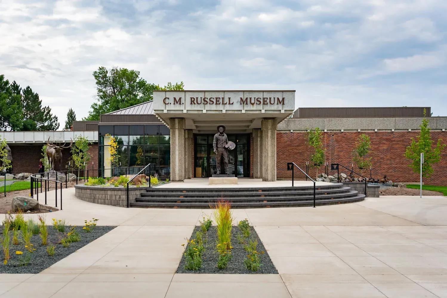 Front entrance of the Russell Museum with stone steps, brick walls, and landscaped flower beds