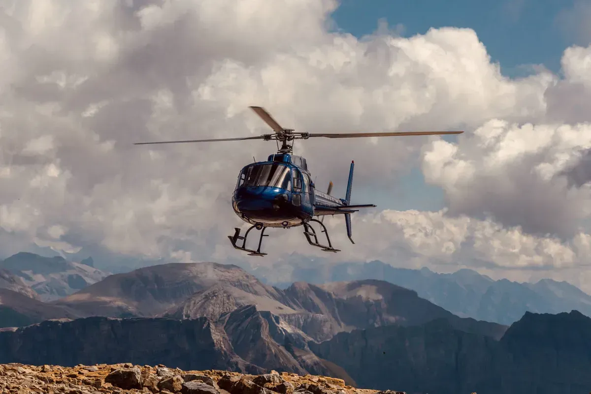 Helicopter flying over rocky mountains beneath cloudy sky