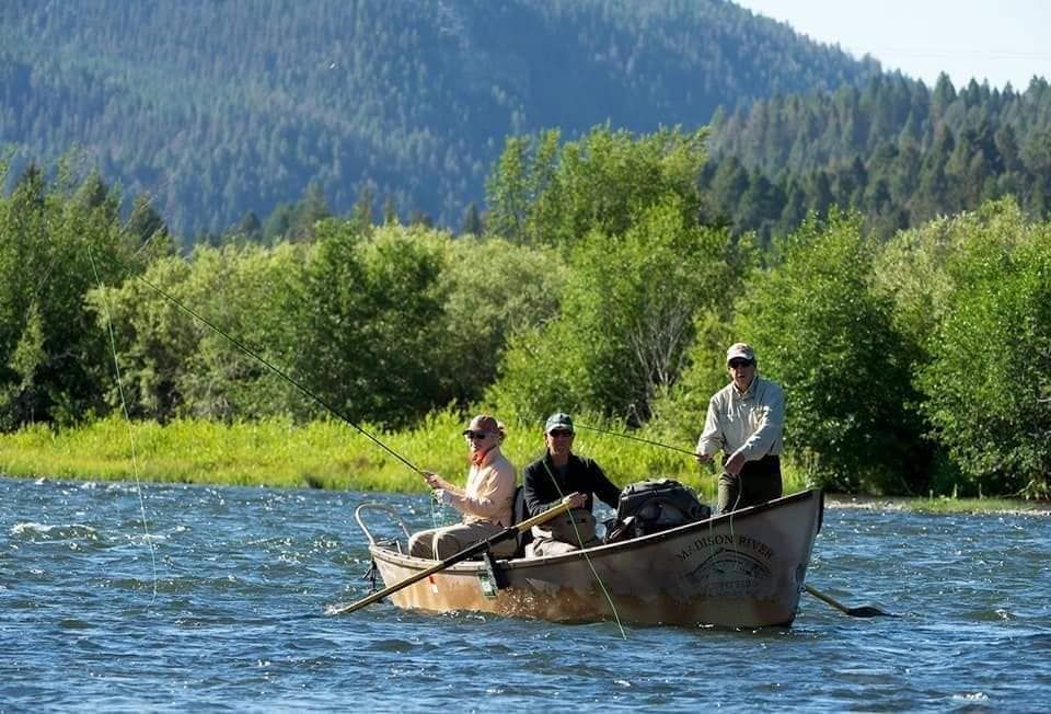 Three people boating on a river with forested mountains in the background