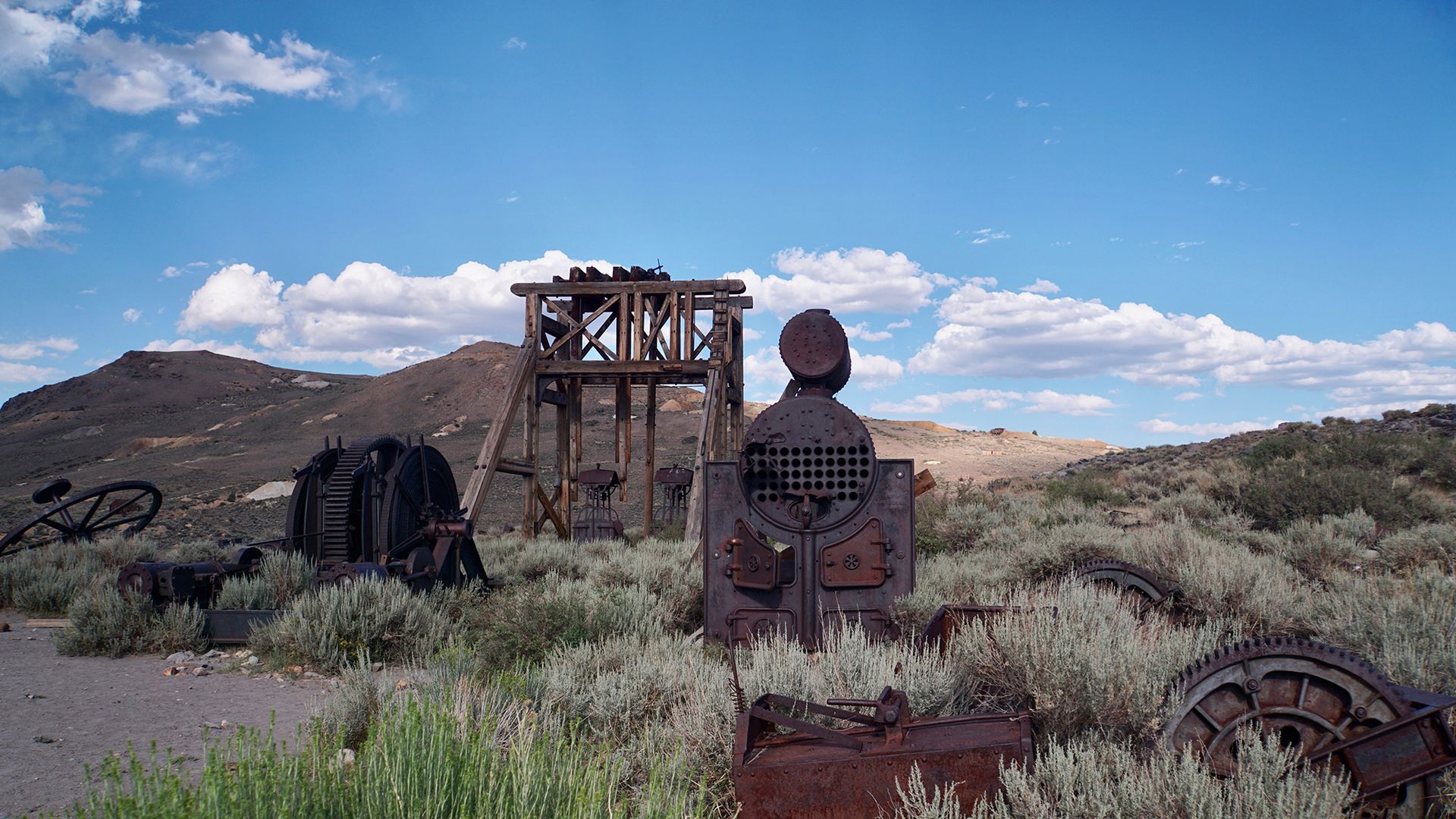 Rusty industrial machinery and old metal structures in a dry desert field under a blue sky with clouds