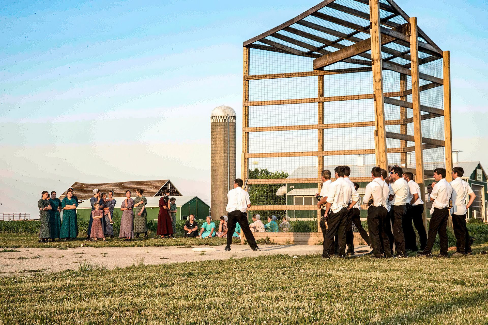 People gathered near a large steel frame building under construction in a grassy field.