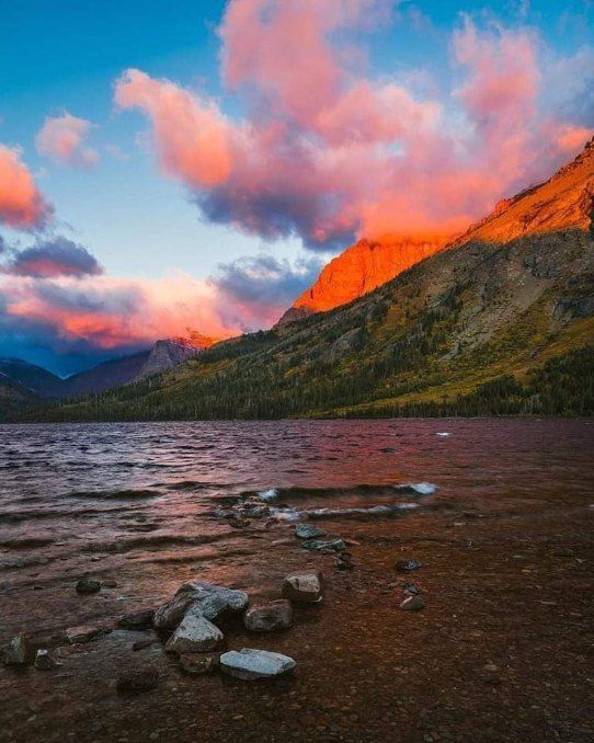 Rocky lakeshore at sunset with pink clouds and orange light on mountain slopes