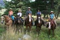 Five horseback riders in helmets pose on a grassy forest trail.