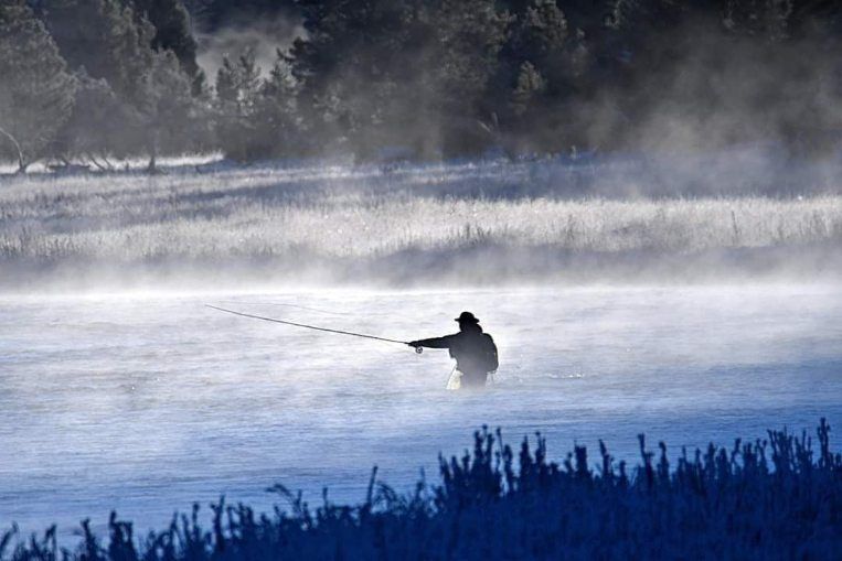 Lone kayaker on a misty river at dawn, silhouetted against blue water and fog