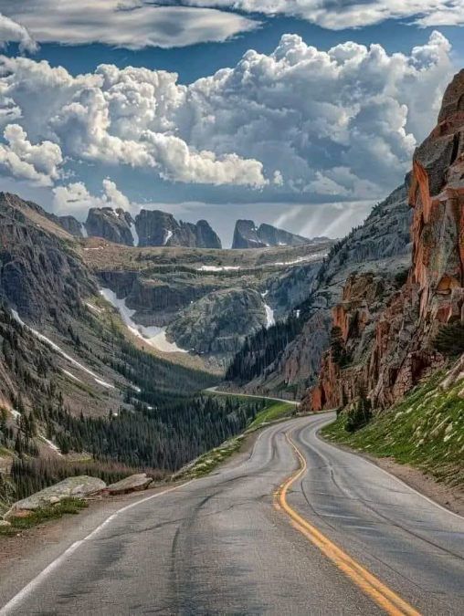Winding mountain road through a dramatic rocky valley under towering clouds