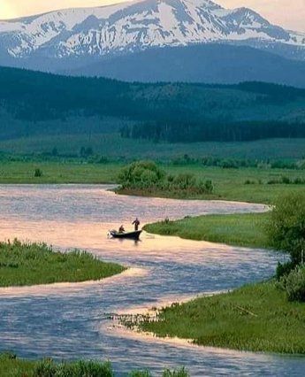 Winding river through green meadows with two canoers, pine forest, and snow-capped mountain in the background