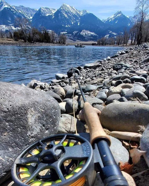 Fishing rod and reel on a rocky lakeshore with snowy mountains and calm water in the background