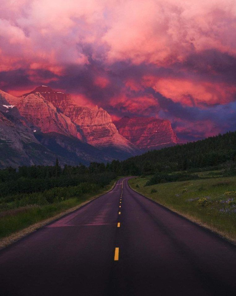 A paved road leading toward mountains under a dramatic pink and purple sunset sky.