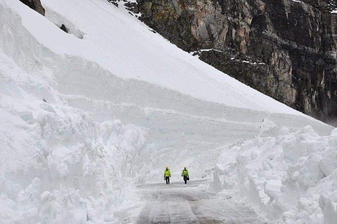 Two hikers in bright jackets walking through a snowy mountain pass surrounded by steep ice walls
