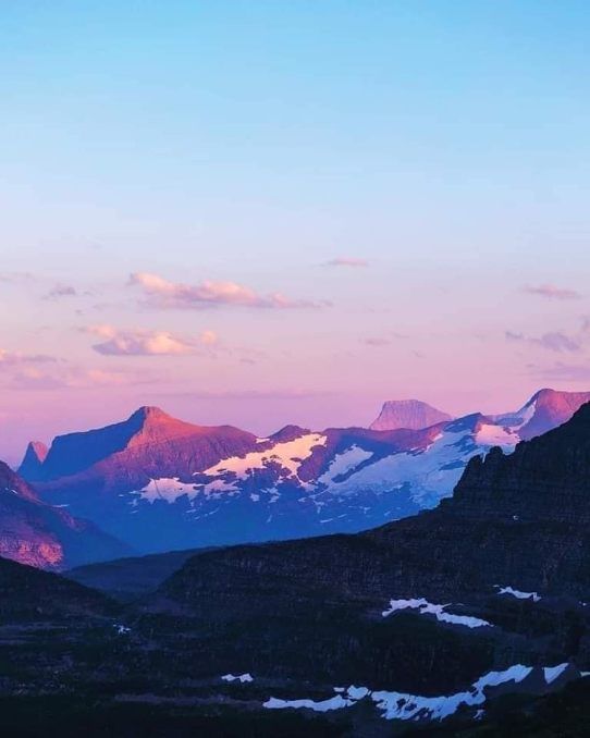 Pink sunrise over snowcapped mountain peaks beneath a clear blue sky.