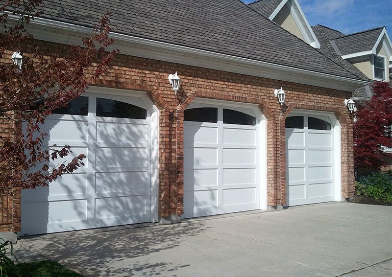 Three-car brick garage with white doors and a paved driveway