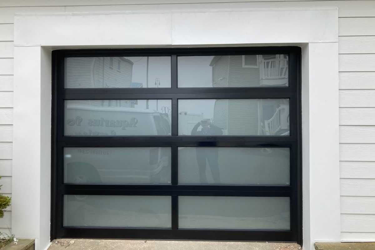 Modern black garage door with frosted glass panels on a white exterior wall