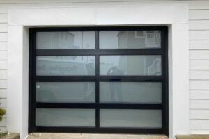 Black garage door with four frosted glass panels in a white exterior wall