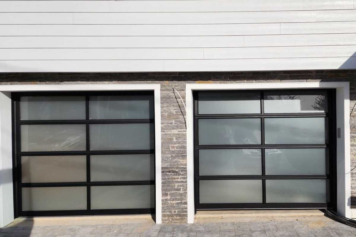 Two black-framed garage doors on a house exterior with white siding and stone trim