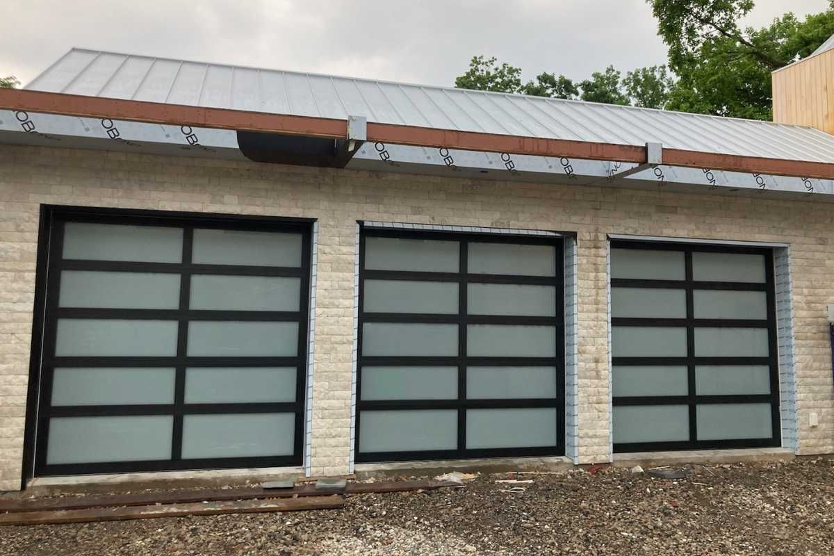 Modern building exterior with three large frosted glass garage doors and a metal roof