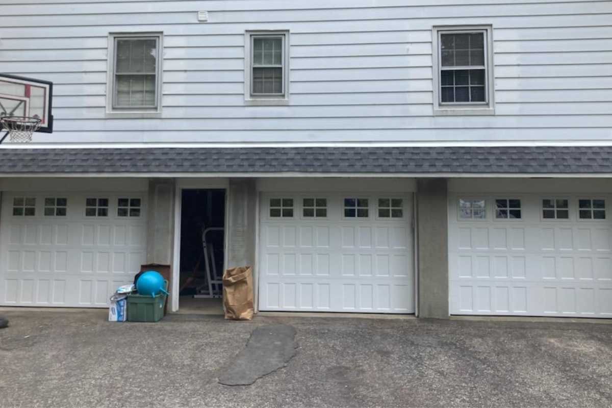 Two-car garage with a brown dog sitting in the open middle doorway next to a blue ball and bucket.