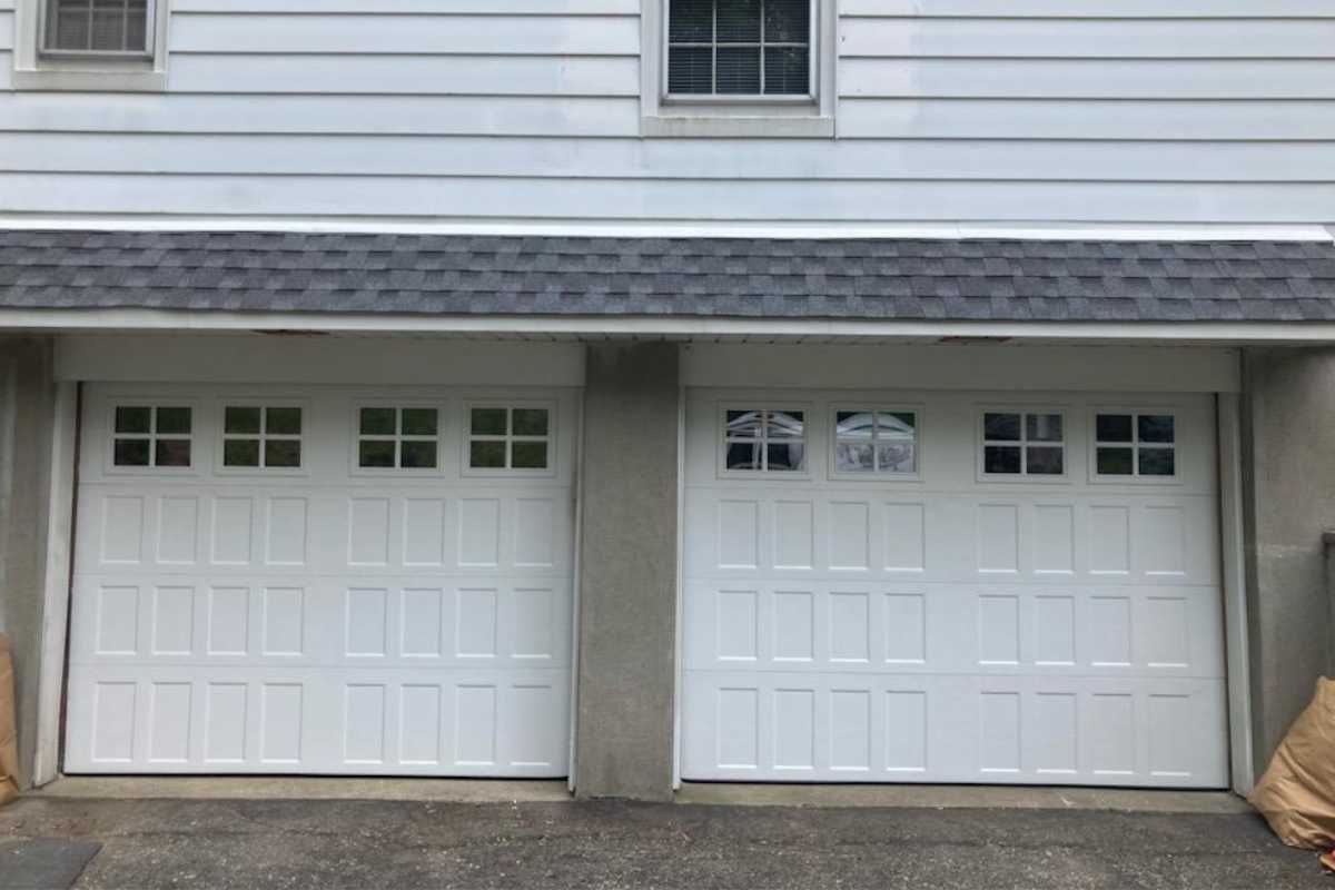 Two white garage doors with small window panes beneath a gray house exterior