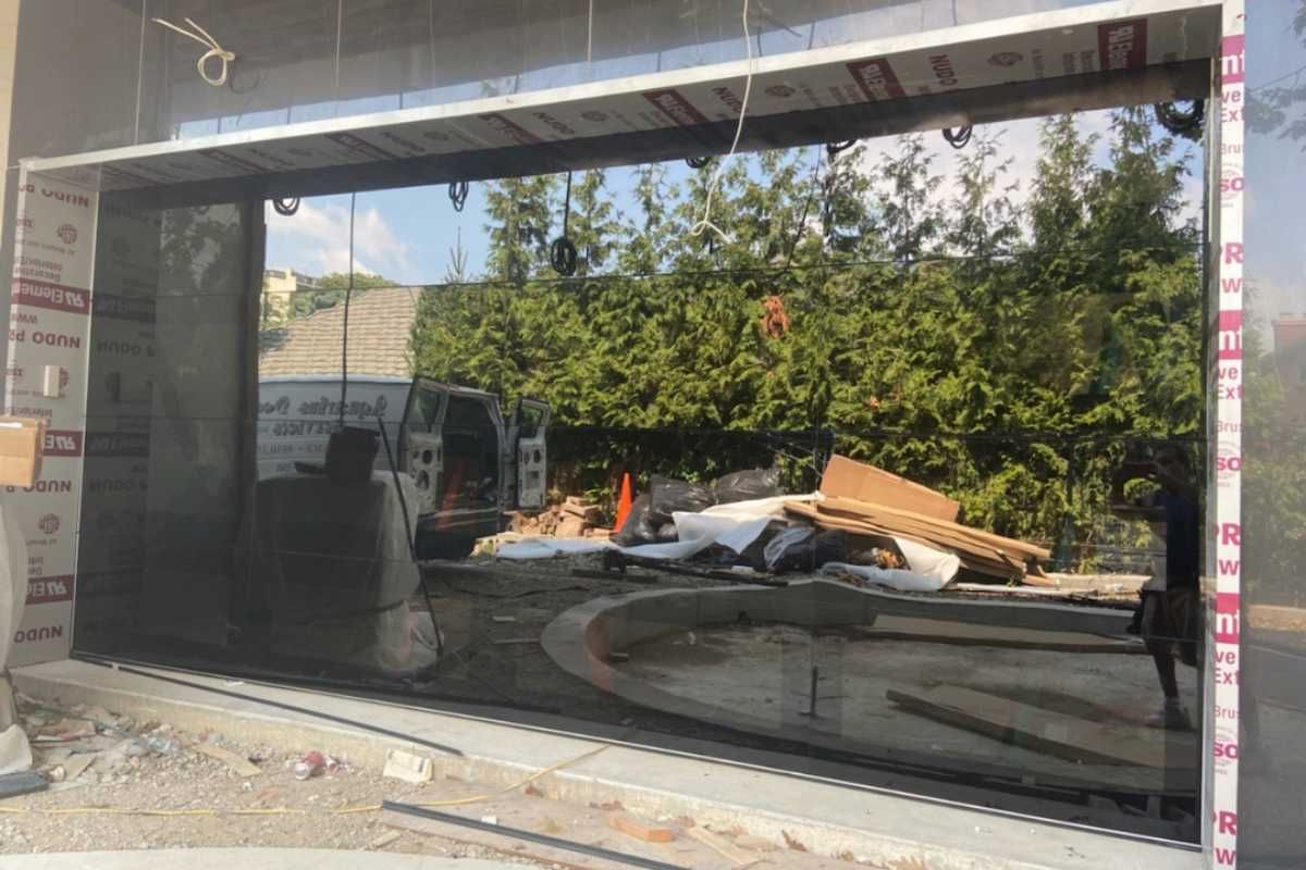 Large black-framed storefront window reflecting a street and showing debris piled inside a closed shop.