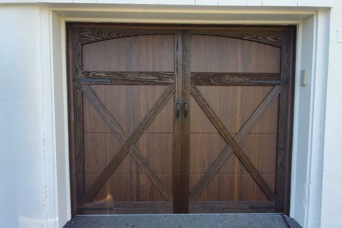 Wooden double garage door with cross-braced panels set in a white stucco wall