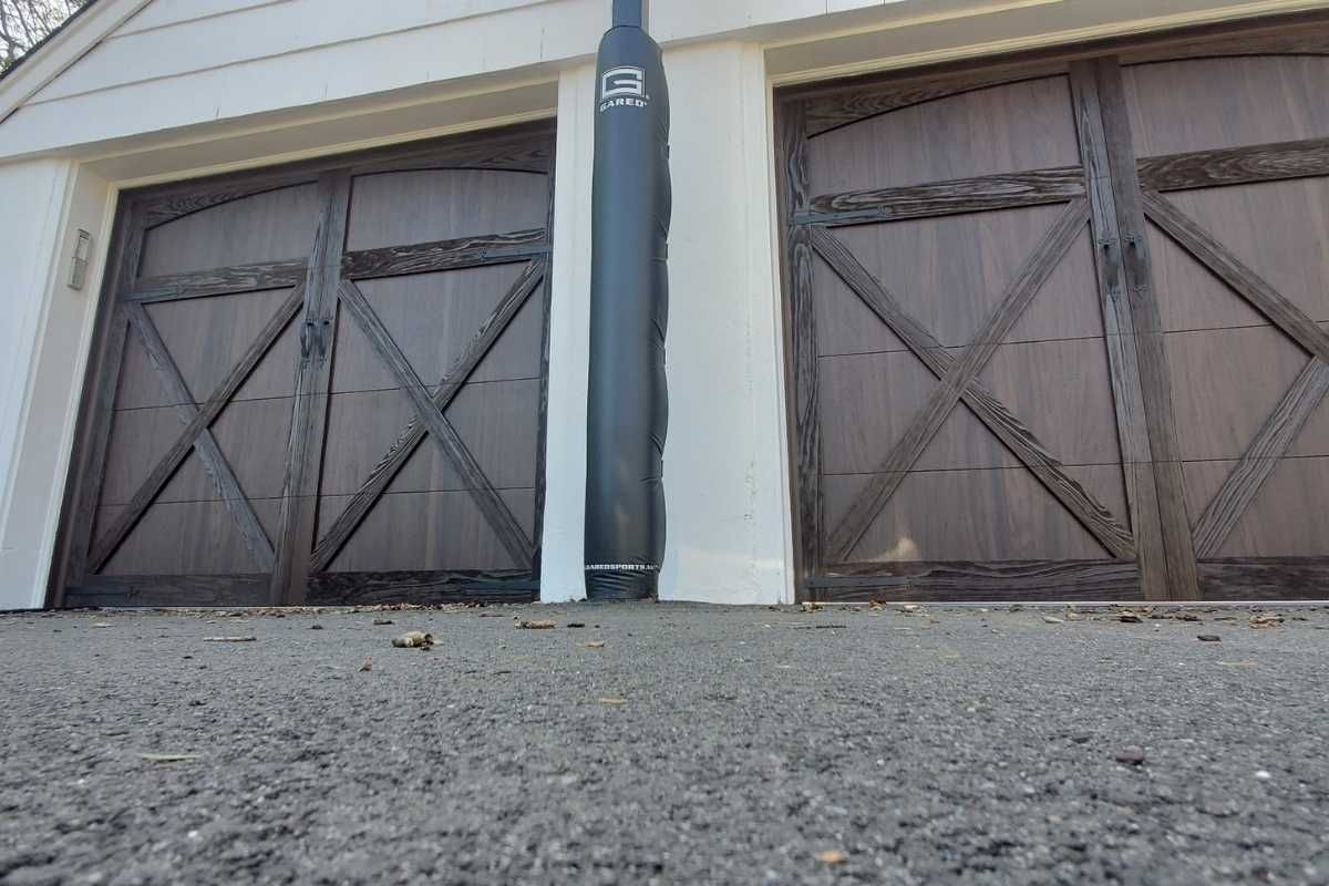 Two wooden garage doors with a central white column and gravel driveway in front